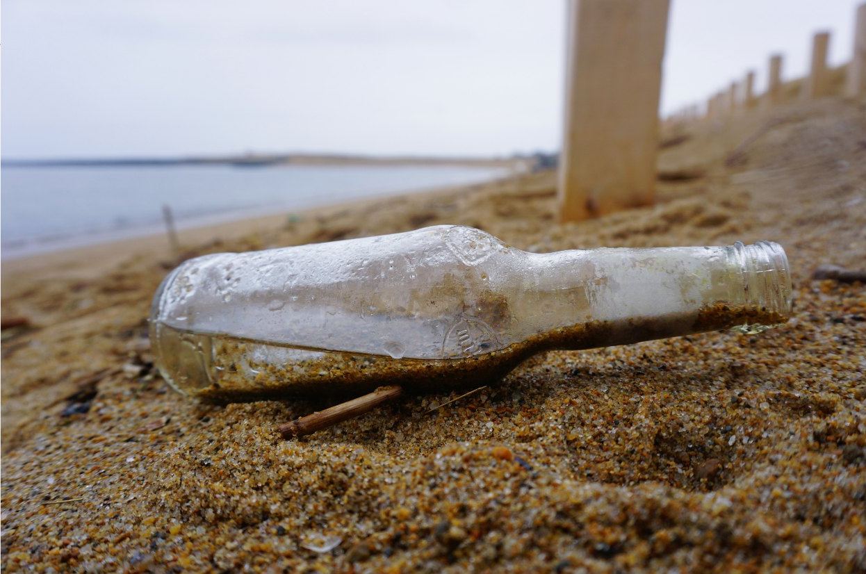 Glass bottleon its side on beach with some water inside