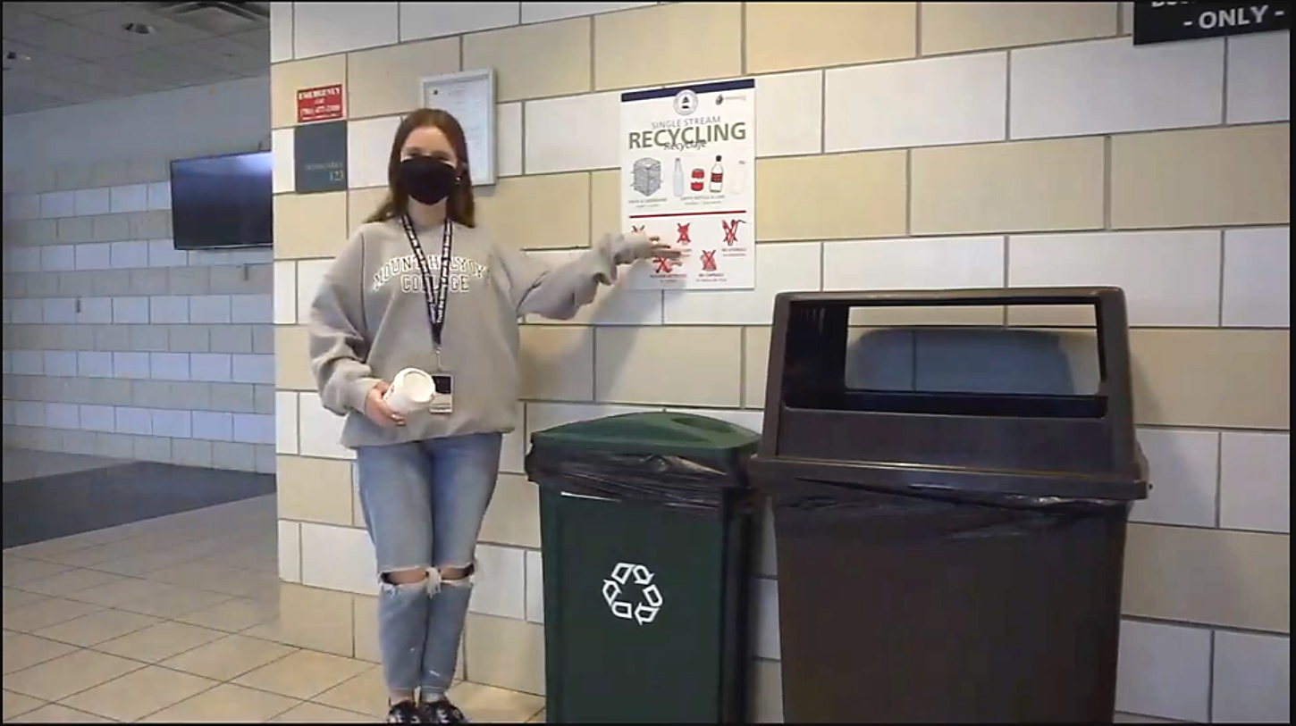 Student in hallway pointing at recycling sign