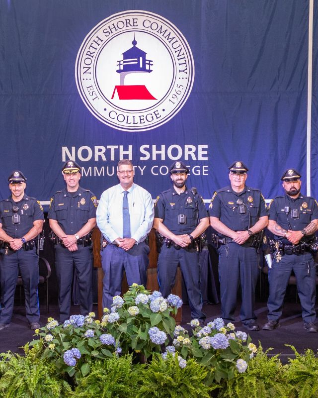 Uniformed campus police officers and maintenance staff posing infront of NSCC flag