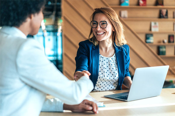 Business women shaking hands over open laptop on table