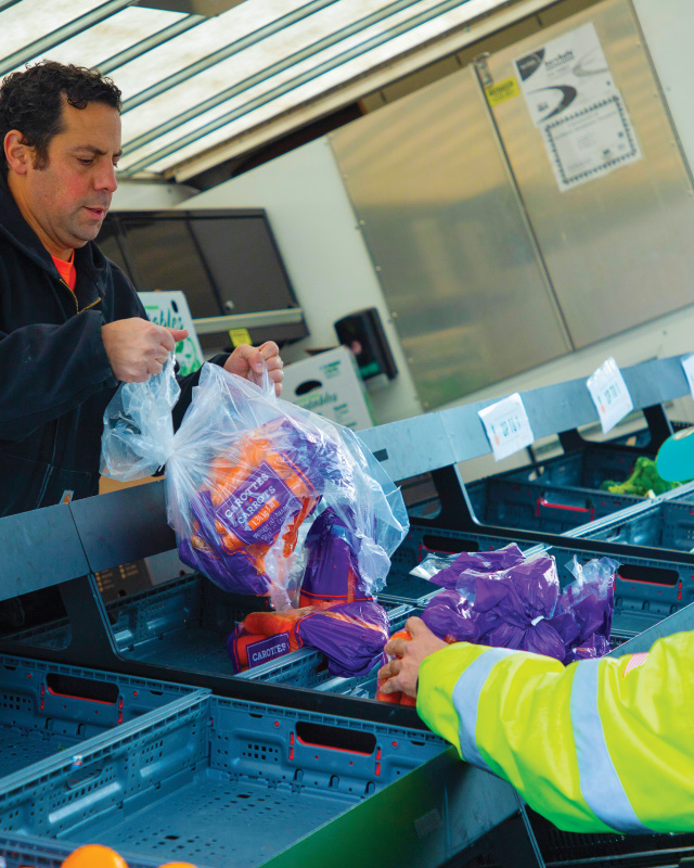 Mobile market staff empty bag of carrots into bin of truck.